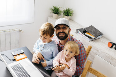 Father working at home, using laptop with his children on his lap - JRFF01984