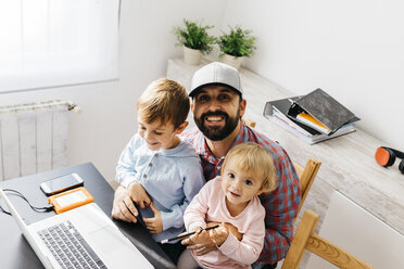 Vater bei der Arbeit zu Hause, mit Laptop und seinen Kindern auf dem Schoß - JRFF01984