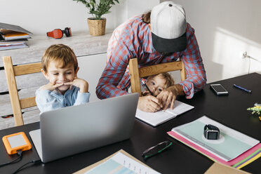 Father writing in notebook while children are playing at his desk - JRFF01994