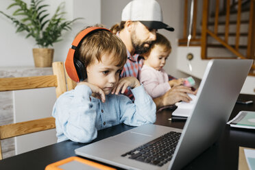 Father working at home, using laptop with his children on his lap - JRFF01996