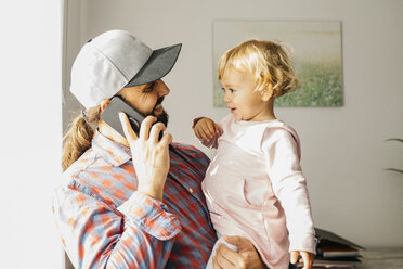 Vater hält seine kleine Tochter auf dem Arm, während er mit seinem Smartphone spricht - JRFF02002