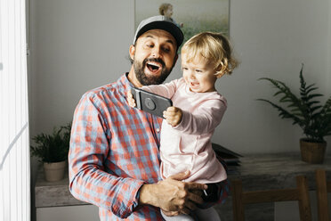 Vater hält seine kleine Tochter auf dem Arm und spielt mit seinem Smartphone - JRFF02003