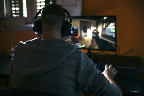 Junger Mann sitzt an seinem PC und spielt Computerspiele, lizenzfreies Stockfoto