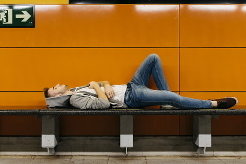 Junger Mann, der auf die U-Bahn wartet und sich auf einer Bank ausruht, lizenzfreies Stockfoto