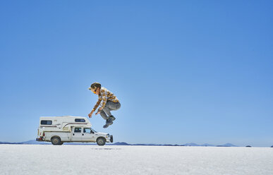 Bolivia, Salar de Uyuni, boy jumping at camper on salt lake - SSCF00019