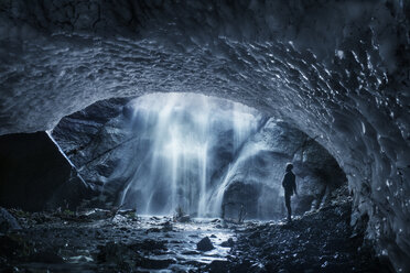 Seitenansicht eines Mannes, der einen Wasserfall betrachtet, während er in einer Eishöhle steht - CAVF55897