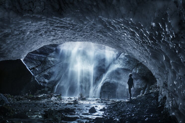 Side view of man looking at waterfall while standing in ice cave - CAVF55897