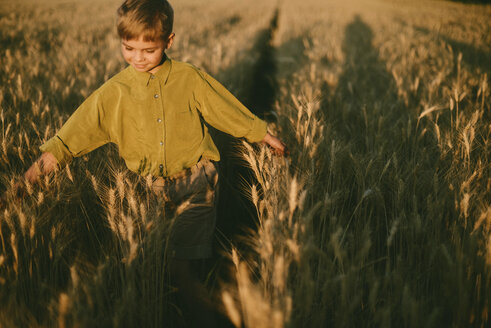 Unbekümmerter Junge spielt inmitten eines Weizenfeldes bei Sonnenuntergang - CAVF55906