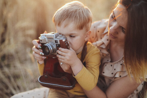 Mutter hilft ihrem Sohn beim Fotografieren mit einer alten Kamera auf einem Feld - CAVF55908
