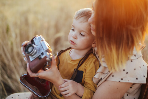 Mutter bringt ihrem Sohn das Fotografieren mit einer alten Kamera auf einem Feld bei, lizenzfreies Stockfoto