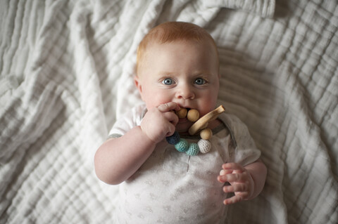 Overhead-Porträt von niedlichen Baby Junge beißt Spielzeug, während auf dem Bett liegend, lizenzfreies Stockfoto