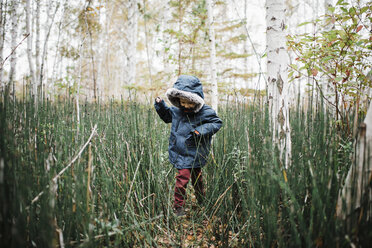 Boy wearing hooded jacket while playing amidst forest - CAVF55969