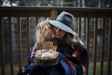 Tochter küsst Mutter und hält Geburtstagskuchen auf dem Balkon - CAVF55978