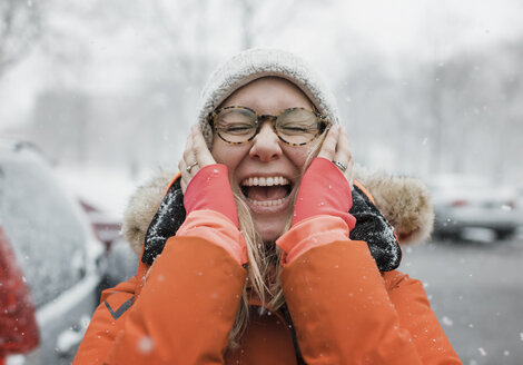 Happy woman with hands on chin screaming while standing on road during snowfall - CAVF55979