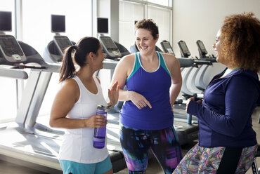 Happy female friends talking while standing in gym - CAVF56002