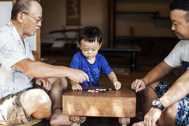 Zwei japanische Männer und ein kleiner Junge sitzen auf dem Boden auf der Veranda eines traditionellen japanischen Hauses und spielen Go. - MINF09578