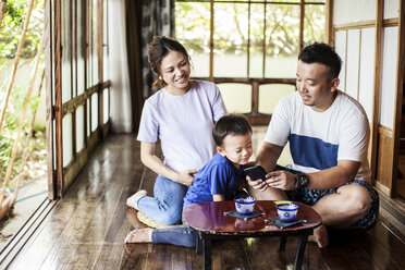 Japanische Frau, Mann und kleiner Junge sitzen auf dem Boden auf der Veranda eines traditionellen japanischen Hauses und trinken Tee. - MINF09582