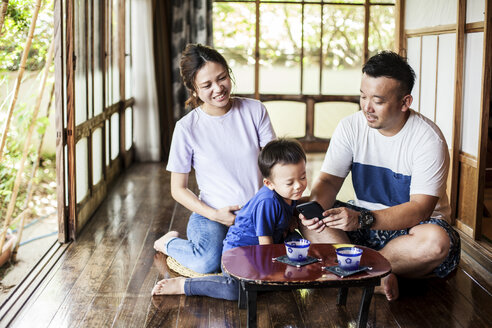 Japanese woman, man and little boy sitting on floor on porch of traditional Japanese house, drinking tea. - MINF09582