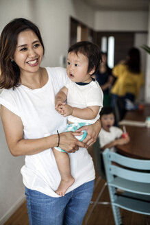Porträt einer japanischen Frau, die mit einem Kleinkind in einem Wohnzimmer steht und in die Kamera lächelt. - MINF09585
