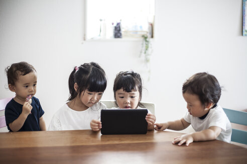 Vier junge japanische Kinder sitzen an einem Tisch und schauen auf ein digitales Tablet. - MINF09588