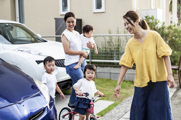 Zwei lächelnde Japanerinnen und drei kleine Kinder stehen neben einem geparkten Auto auf einer Straße. - MINF09592