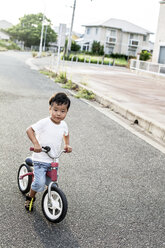 Porträt eines japanischen Jungen, der auf der Straße mit einem Fahrrad spielt und in die Kamera schaut. - MINF09593