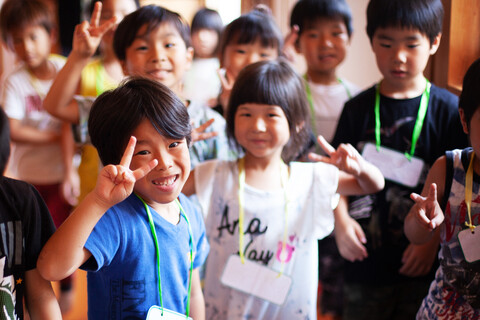 Eine Gruppe lächelnder Kinder in einer japanischen Vorschule, die ein Friedenszeichen machen und in die Kamera schauen., lizenzfreies Stockfoto
