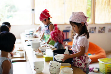 A girl and a boy wearing headscarves standing at a table in a Japanese preschool, serving lunch. - MINF09626