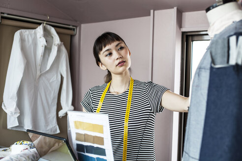 Japanische Modedesignerin bei der Arbeit in ihrem Atelier, betrachtet ein Kleidungsstück auf einem Schneidermodell. - MINF09653