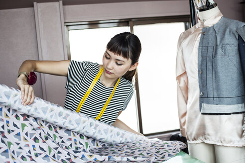 Japanische Modedesignerin bei der Arbeit in ihrem Atelier, in der Hand eine Stoffrolle. - MINF09654