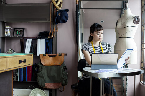 Japanische Modedesignerin bei der Arbeit in ihrem Atelier, am Tisch sitzend, mit Blick auf Stoffmuster. - MINF09655