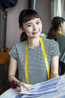 Eine japanische Modedesignerin arbeitet in ihrem Atelier und lächelt in die Kamera. - MINF09658