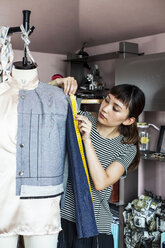 Japanische Modedesignerin bei der Arbeit an einem Kleidungsstück an einem Schneidermodell in einem Atelier. - MINF09659