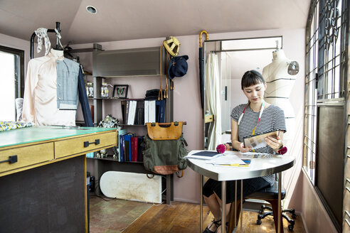 Japanische Modedesignerin sitzt am Schreibtisch und arbeitet in ihrem Atelier. - MINF09664