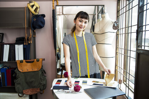 Eine japanische Modedesignerin arbeitet in ihrem Atelier und lächelt in die Kamera. - MINF09666