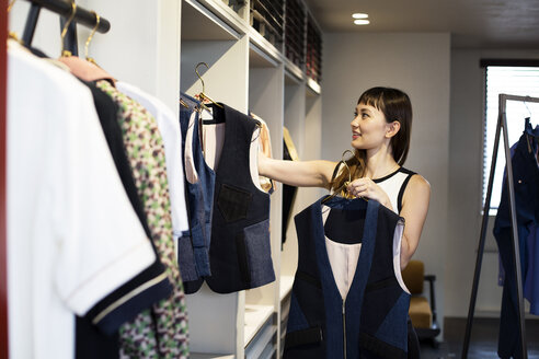 Eine japanische Verkäuferin steht in einem Bekleidungsgeschäft und hängt blaue Westen auf eine Stange. - MINF09678