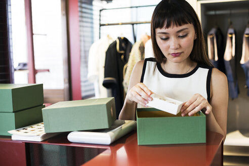 Japanische Verkäuferin, die in einem Bekleidungsgeschäft am Tresen steht und Schmuck in eine grüne Schachtel legt. - MINF09680