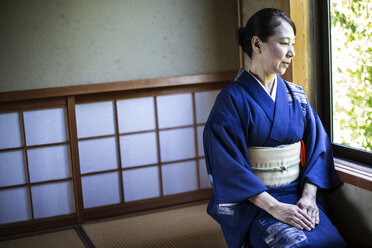 Japanische Frau in traditionellem hellblauem Kimono mit cremefarbenem Obi kniend auf dem Boden in einem traditionellen japanischen Haus. - MINF09687