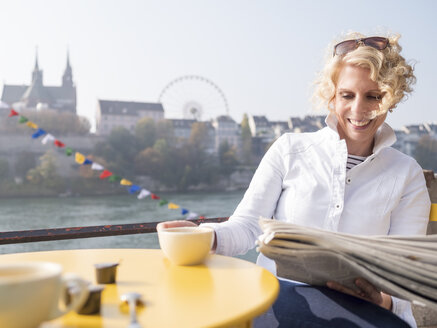 Schweiz, Basel, lächelnde Frau liest Zeitung in einem Straßencafé am Rhein - LAF02166