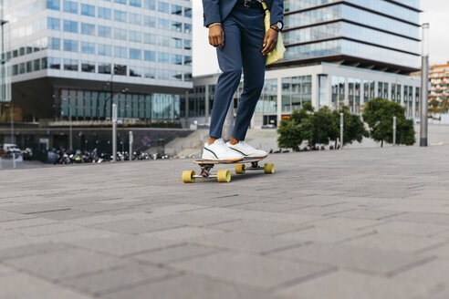 Spain, Barcelona, legs of young businessman riding skateboard in the city - JRFF02039