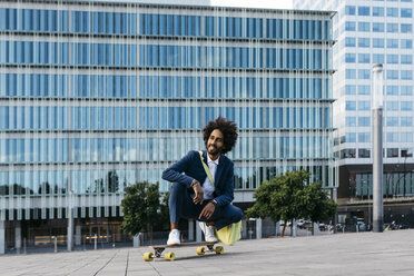 Spanien, Barcelona, junger Geschäftsmann hockt auf einem Skateboard in der Stadt - JRFF02040