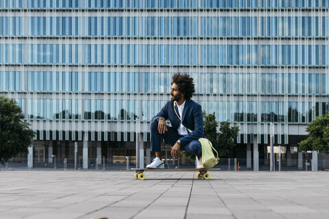 Spain, Barcelona, young businessman crouching on skateboard in the city stock photo