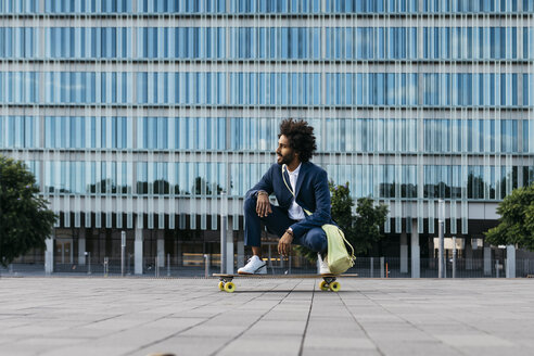 Spanien, Barcelona, junger Geschäftsmann hockt auf einem Skateboard in der Stadt - JRFF02041