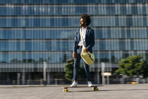 Spain, Barcelona, young businessman riding skateboard in the city - JRFF02042
