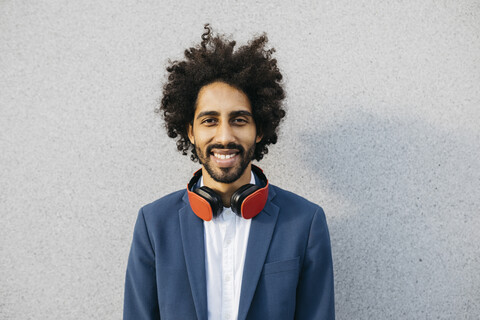 Portrait of smiling young businessman with headphones at a wall stock photo