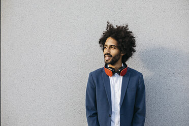 Smiling young businessman with headphones at a wall - JRFF02059