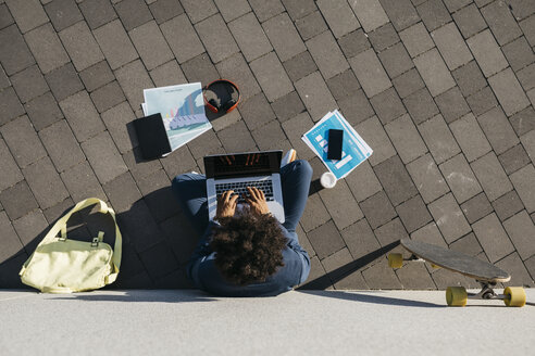 Junger Geschäftsmann sitzt im Freien an einer Wand und arbeitet an einem Laptop - JRFF02062