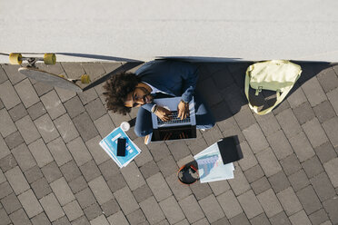 Junger Geschäftsmann sitzt im Freien an einer Wand und arbeitet an einem Laptop - JRFF02063