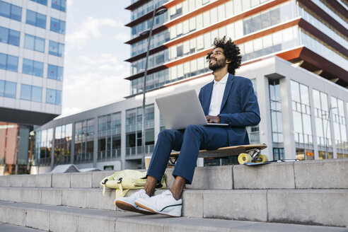 Spain, Barcelona, young businessman sitting outdoors in the city working on laptop - JRFF02065