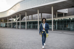 Spanien, Barcelona, junger Geschäftsmann verlässt Bürogebäude mit Skateboard in der Stadt - JRFF02080